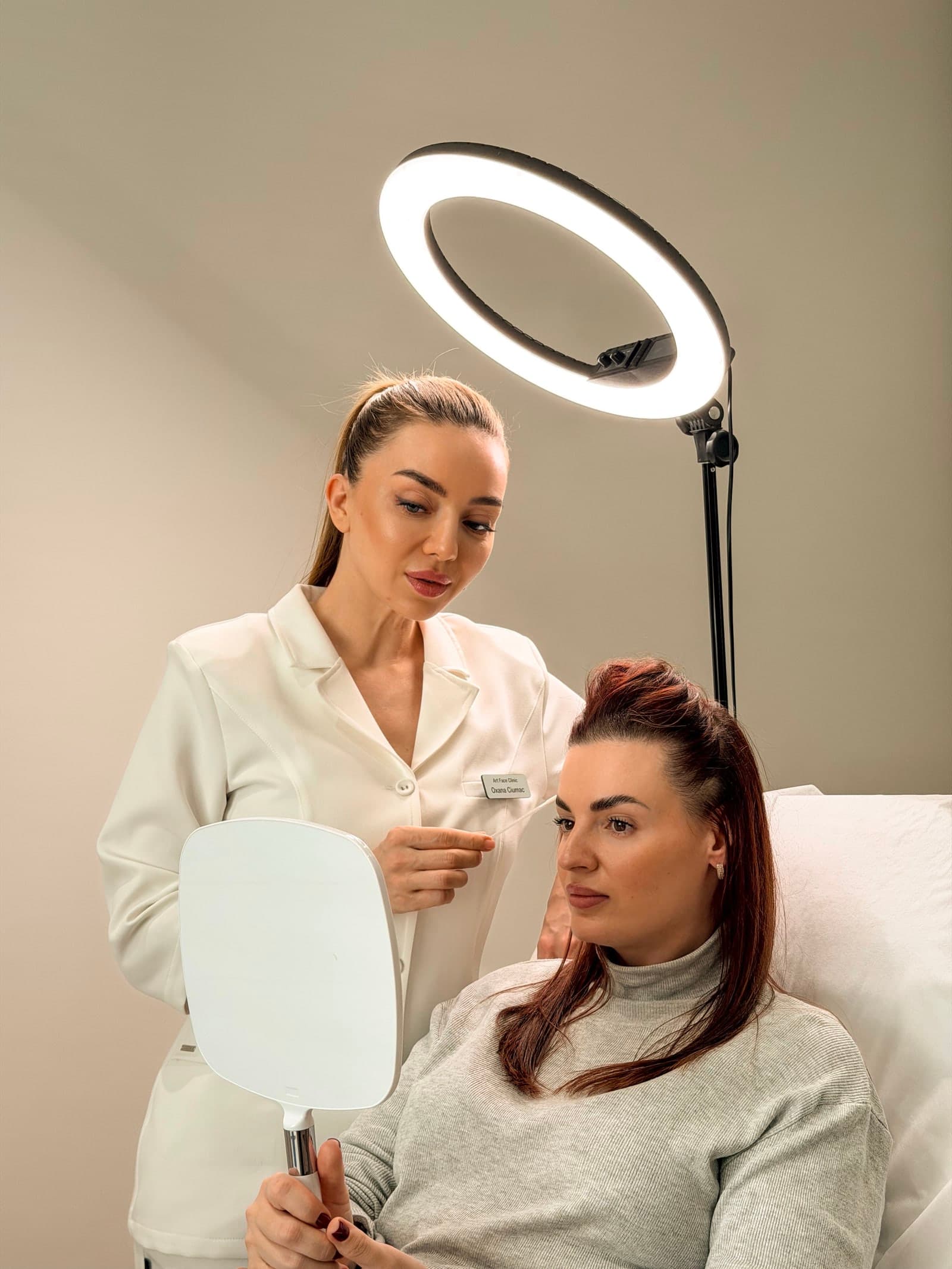 Practitioner and client reviewing the brows in a hand mirror during a pigment removal consultation at ART FACE Clinic