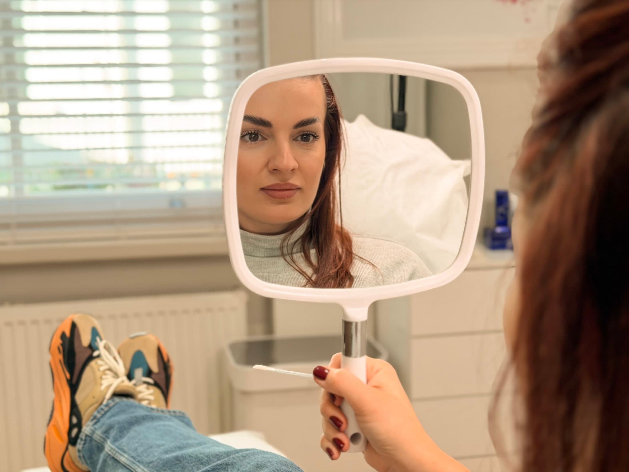Client reviewing the treated brows in a hand mirror after laser pigment removal at ART FACE Clinic